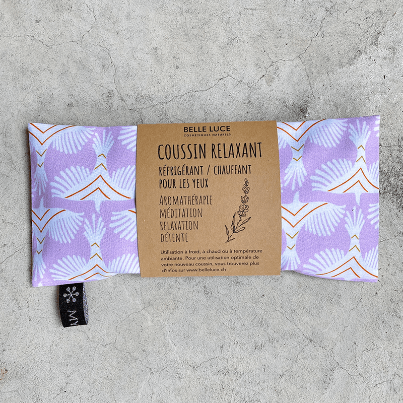 Coussin relaxant pour les yeux de la marque Belle Luce, au motif violet et orange avec des motifs géométriques. Ce coussin est utilisé pour la relaxation, l'aromathérapie et la méditation, offrant des options réfrigérantes ou chauffantes. L'emballage met en avant ses bienfaits de détente. Des brins de lavande sont posés à côté, soulignant le lien avec l'aromathérapie