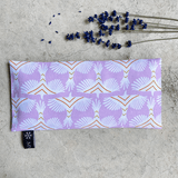 Coussin relaxant pour les yeux de la marque Belle Luce, au motif violet et orange avec des motifs géométriques. Ce coussin est utilisé pour la relaxation, l'aromathérapie et la méditation, offrant des options réfrigérantes ou chauffantes. L'emballage met en avant ses bienfaits de détente. Des brins de lavande sont posés à côté, soulignant le lien avec l'aromathérapie