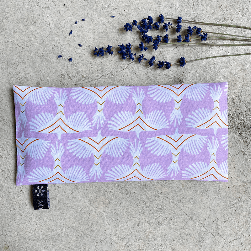 Coussin relaxant pour les yeux de la marque Belle Luce, au motif violet et orange avec des motifs géométriques. Ce coussin est utilisé pour la relaxation, l'aromathérapie et la méditation, offrant des options réfrigérantes ou chauffantes. L'emballage met en avant ses bienfaits de détente. Des brins de lavande sont posés à côté, soulignant le lien avec l'aromathérapie